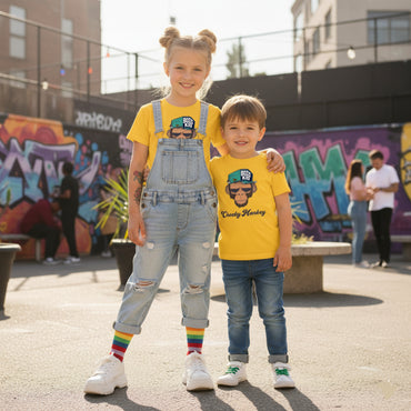 Two children wearing yellow t-shirts with graphic designs, standing in front of a graffiti-covered wall.