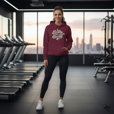Woman in a maroon hoodie with text standing in a gym with a cityscape view.