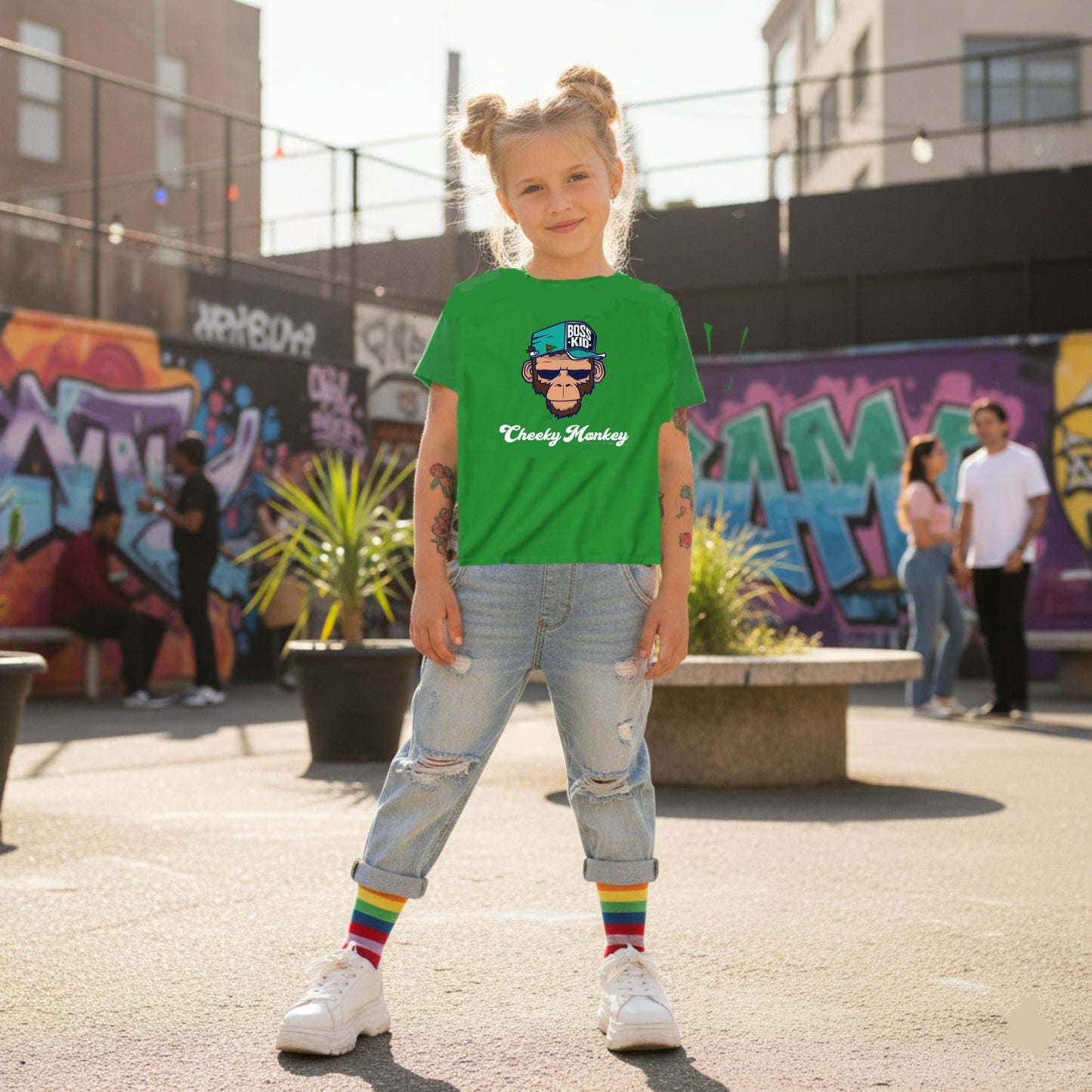 Child wearing a green t-shirt with a graphic design, standing in an urban setting with graffiti.