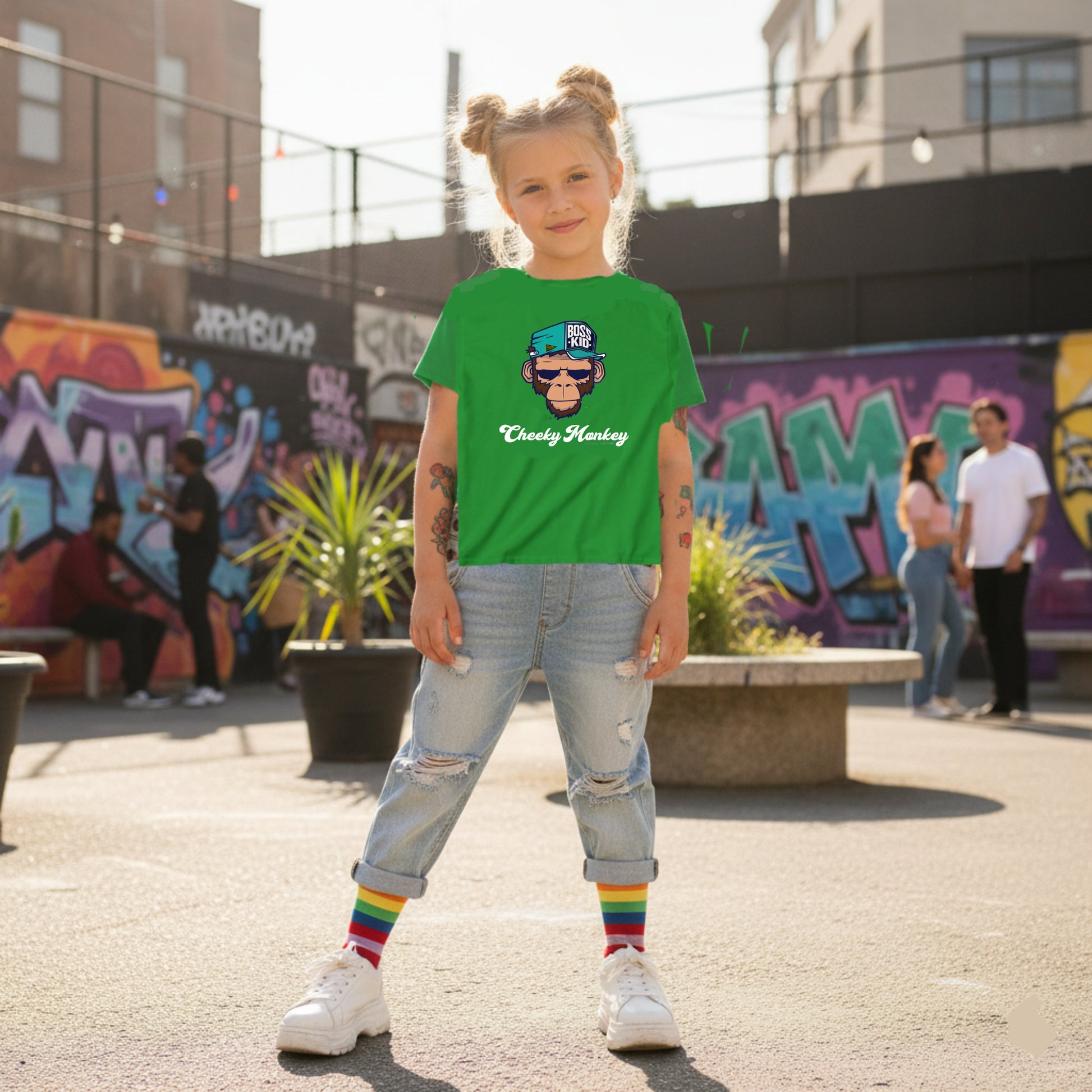 Child wearing a green t-shirt with a graphic design, standing in an urban setting with graffiti.
