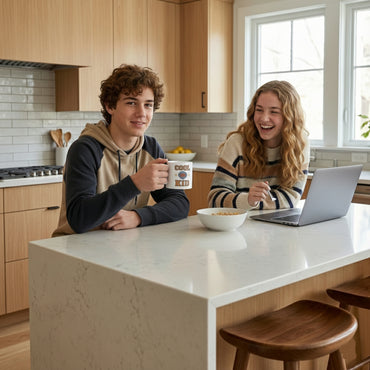 Two people sitting at a kitchen island with a laptop and a bowl of cereal.