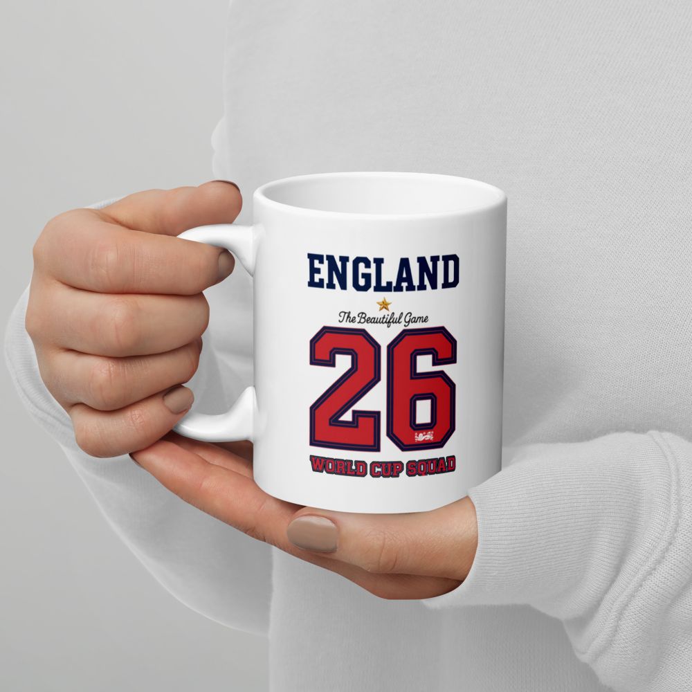White mug with 'England' and number '26' printed on it, held by a person against a light gray background.