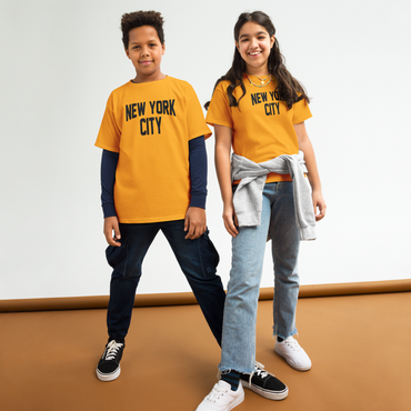 Two children wearing 'New York City' t-shirts standing on a brown surface with a white background.