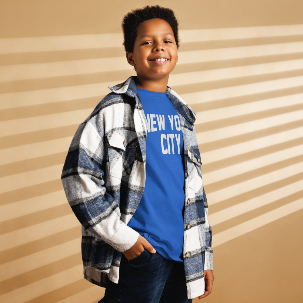 Child wearing a blue 'New York City' t-shirt with a plaid shirt over it against a striped background