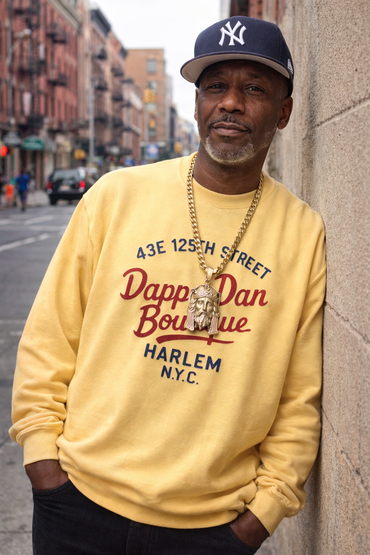 Man wearing a yellow sweatshirt with 'Dapp'dan Boutique' text, standing on a city street.