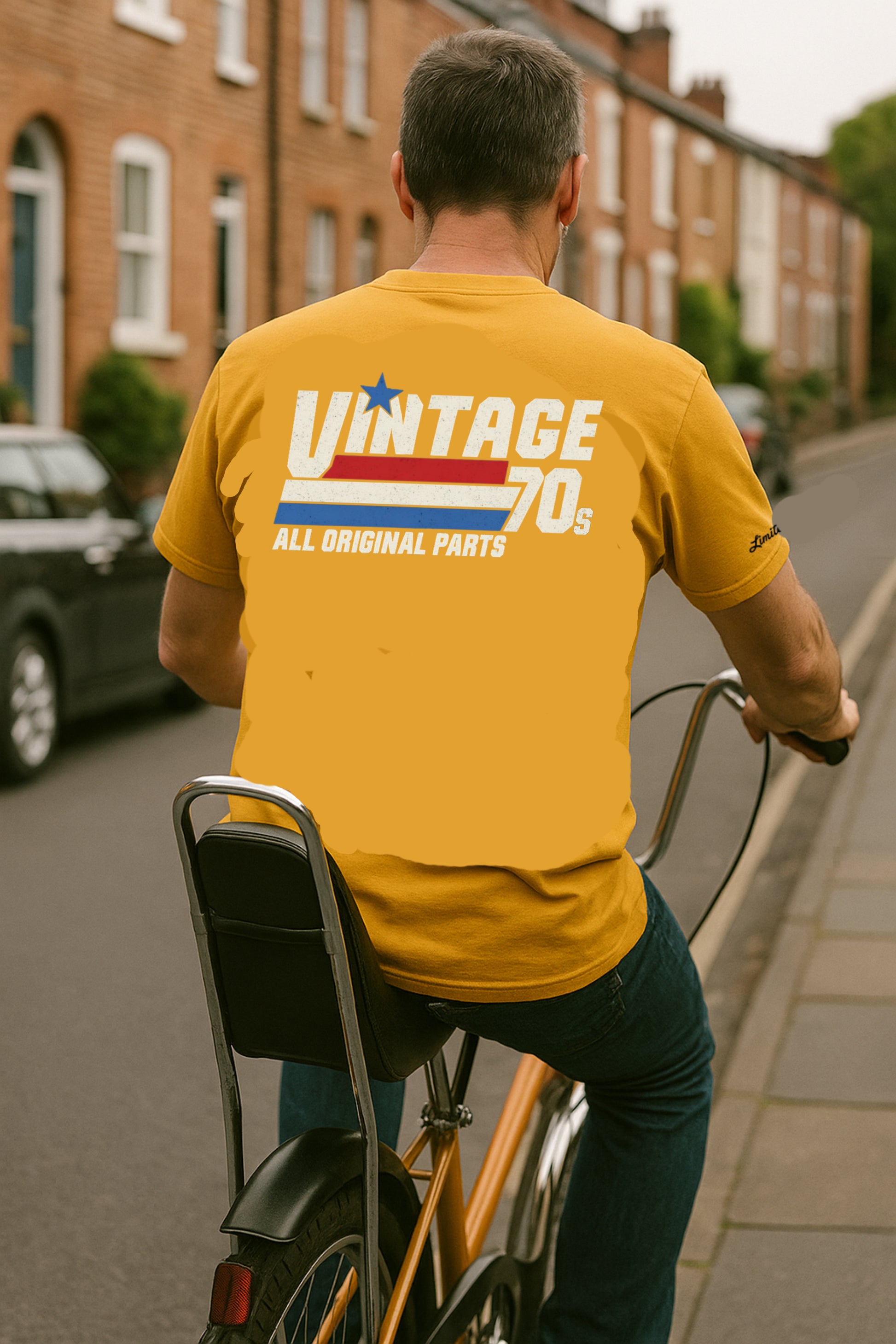 Man riding a bicycle wearing a yellow 'Vintage 70s' t-shirt on a residential street.