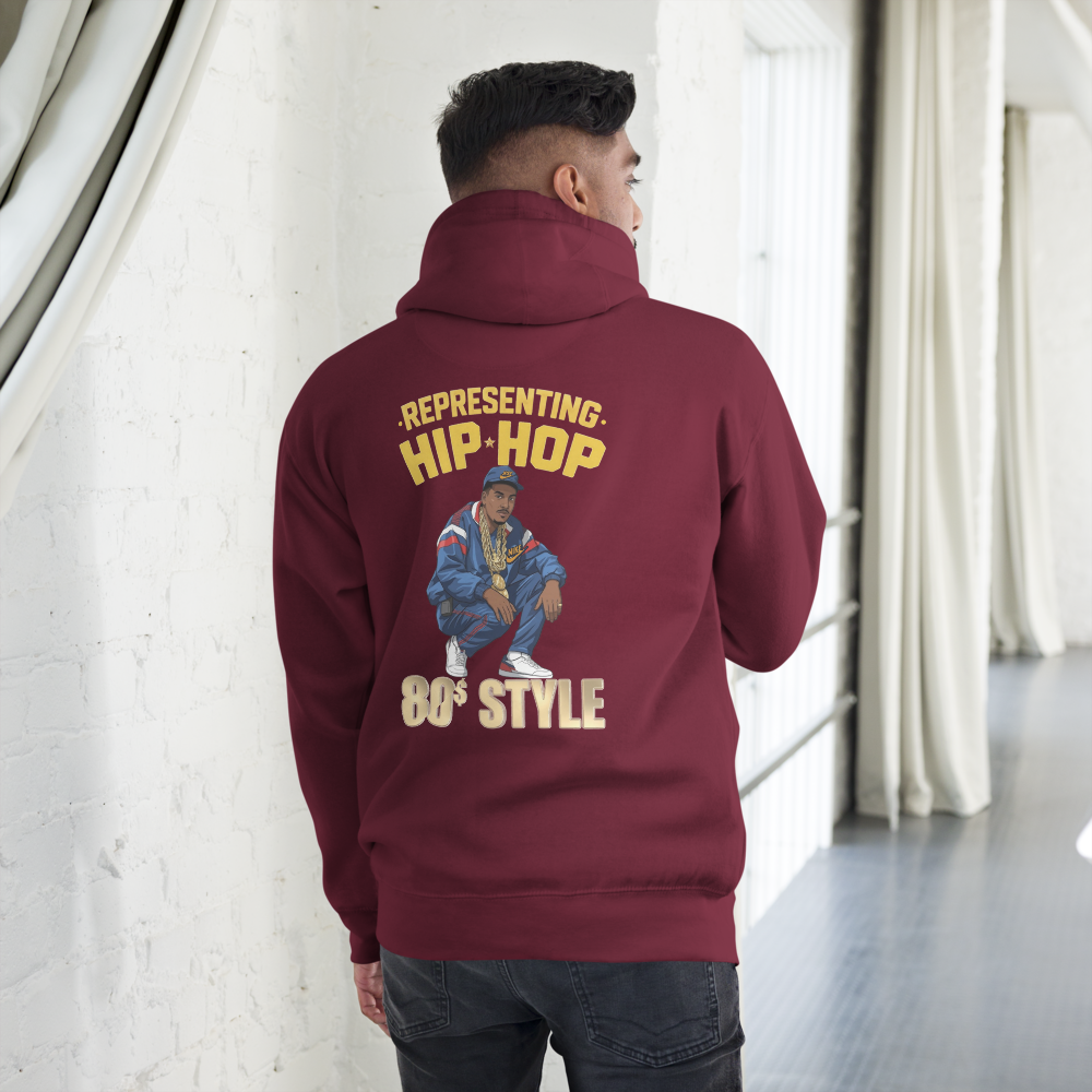 Person wearing a maroon hoodie with a graphic and text on the back, standing in a room with white walls and curtains.