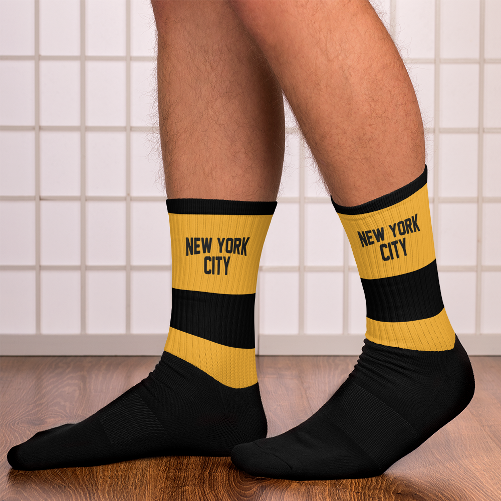Black and yellow socks with 'New York City' text worn indoors on a tiled floor.