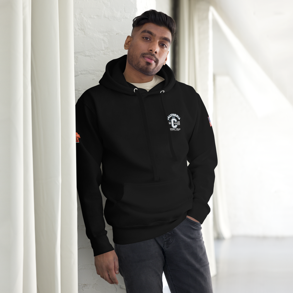 Man wearing a black hoodie with a logo, standing against a white wall.
