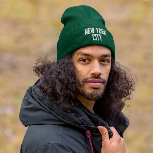 Man wearing a green 'New York City' beanie with a blurred natural background