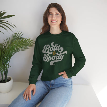 Woman wearing a green sweatshirt with 'Bold & Sporty' text, sitting on a white surface with a plant in the background.