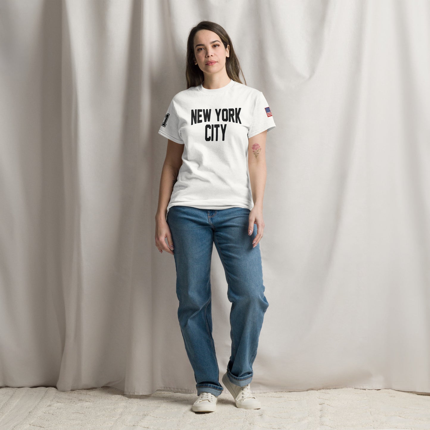 Person wearing a white 'New York City' t-shirt and blue jeans against a plain background