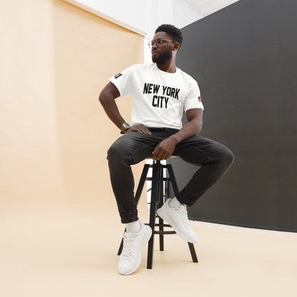 Man sitting on a stool wearing a 'New York City' t-shirt against a plain background